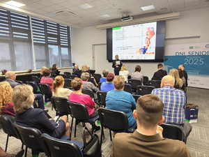 Zdjęcie przedstawia policjantkę stojącą przed siedzącymi na krzesłach ludźmi.
