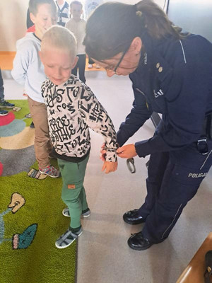 Zdjęcie przedstawia policjantkę, która zakłada kajdanki chłopcu.