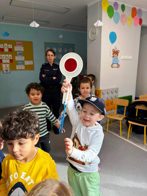 Zdjęcie przedstawia policjantkę stojącą z dziećmi. Jedno dziecko otrzyma w uniesionej ręce tarcz e do zatrzymywania pojazdów.
