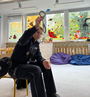 Zdjęcie przedstawia policjantkę, która trzyma w uniesionej ręce kajdanki.