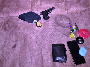 Zdjęcie przedstawia przedmiot przypominający broń, portfel, telefon leżące na łóżku.