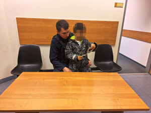 Zdjęcie przedstawia policjanta opiekującego się małym chłopcem, bawiącym się kajdankami.