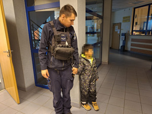 Zdjęcie przedstawia policjanta trzymającego za rękę małe dziecko.