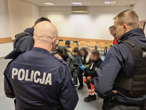 Zdjęcie przedstawia policjantów i ratownika medycznego stojących przy rodzinie z dzieckiem.