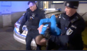 Zdjęcie przedstawia dwóch policjantów prowadzących zatrzymanego.