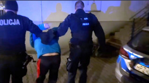 Zdjęcie przedstawia dwóch policjantów prowadzących zatrzymanego.