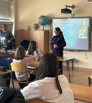 Zdjęcie przedstawia policjantkę stojącą przed uczniami siedzącymi w szkolnych ławkach.