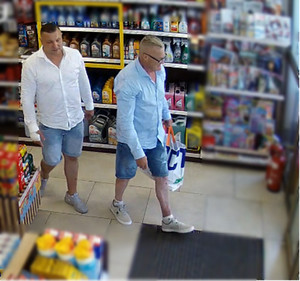 Zdjęcie przedstawia dwóch ubranych w jasne koszule i granatowe spodenki o długości do kolan mężczyzn wewnątrz sklepu.