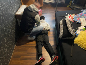 Zdjęcie przedstawia policjanta pochylającego się nad leżącym na podłodze mężczyzną.