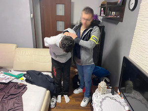 Zdjęcie przedstawia policjanta prowadzącego pochylającego się do przodu zatrzymanego.