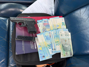 Zdjęcie przedstawia gotówkę oraz przedmiot przypominający broń leżące na siedzeniu w samochodzie.