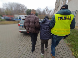 Zdjęcie przedstawia policjantów, którzy prowadzą przez dziedziniec, pomiędzy sobą zatrzymanego mężczyznę.