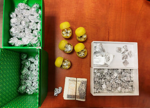 Zdjęcie przedstawia srebrne zawiniątka, gotówkę znajdujące się w pojemnikach i na brązowym blacie stołu.