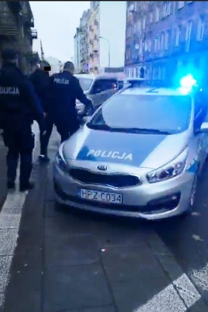 Zdjęcie przedstawia dzielnicowych, którzy prowadzą do radiowozu zatrzymanego mężczyznę.