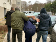 Zdjęcie przedstawia policjantów w ubraniach cywilnych, prowadzących pomiędzy sobą zatrzymanego w kajdankach.