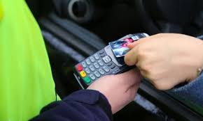 Zdjęcie przedstawia dłoń z kartą przy terminalu płatniczym.