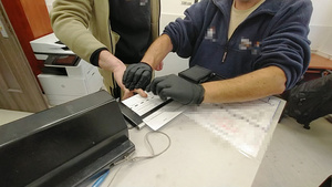 Zdjęcie przedstawia policyjnego technika pobierającego odciski palców mężczyźnie.