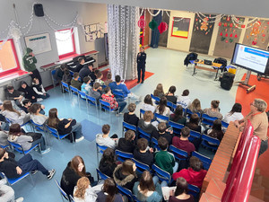 Zdjęcie przedstawia policjantkę stojącą przed uczniami siedzącymi na krzesłach.