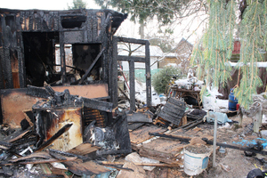 Zdjęcie przedstawia spalony domek działkowy i jego otoczenie.