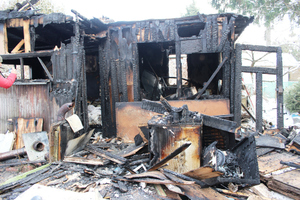 Zdjęcie przedstawia spalony domek działkowy i jego otoczenie.