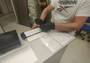 Zdjęcie przedstawia mężczyznę w czarnych rękawiczkach ochronnych, który wykonuje odciski palców innej osobie.