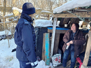 Zdjęcie przedstawia policjanta rozmawiającego z mężczyzną stojącym przed prowizorycznym pomieszczeniem.