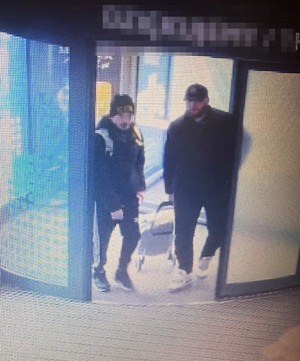 Zdjęcie przedstawia dwóch ubranych n ciemno mężczyzn wchodzących do galerii handlowej.