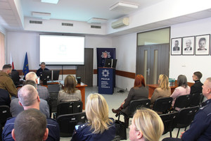 Zdjęcie przedstawia policjantów siedzących na sali. Przed nimi stoi umundurowany policjant.