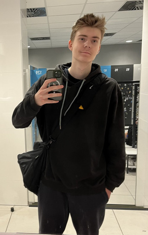 Zdjęcie przedstawia ubranego na ciemno chłopaka trzymającego telefon w ręku.