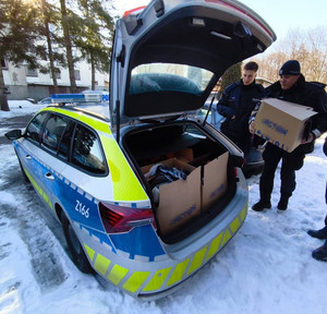 Zdjęcie przedstawia policjantów wkładających do bagażnika radiowozu kartony.