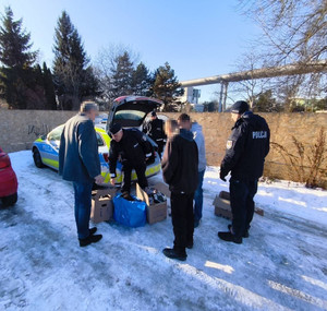 Zdjęcie przedstawia policjantów stojących z mężczyznami wokół radiowozu i ułożonych kartonów.