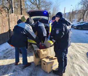 Zdjęcie przedstawia policjantów stojących z mężczyznami wokół radiowozu i ułożonych kartonów.