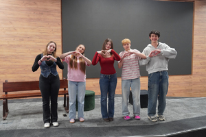 Zdjęcie przedstawia uczniów stojących na scenie i układających dłonie w serca.