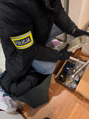 Zdjęcie przedstawia policjanta, z opaską POLICJA na przedramieniu, który trzyma w dłoniach narkotyki.