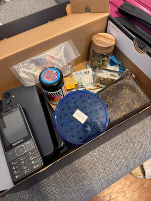 Zdjęcie przedstawia opakowanie zawierające różne pojemniki z zabronionymi substancjami oraz telefon komórkowy.