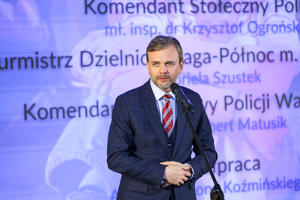 Zdjęcie przedstawia mężczyznę przed mikrofonem.