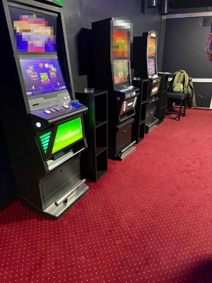 Zdjęcie przedstawia trzy automaty do gier hazardowych, umieszczone w pomieszczeniu przy ścianie.