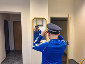 Zdjęcie przedstawia chłopaka ubranego w niebieską bluzę. który przed lustrem przymierza policyjną czapkę.