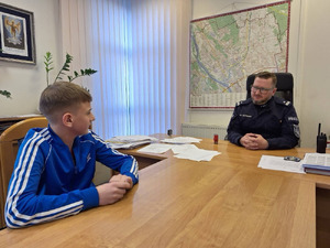 Zdjęcie przedstawia policjanta i nastolatka siedzących przy jednym stole w gabinecie.