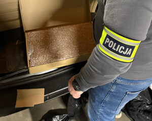 Zdjęcie przedstawia policjanta stojącego obok samochodu, w bagażniku którego znajdują się kartony.