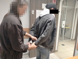 Zdjęcie przedstawia policjantkę, w ubraniach cywilnych, która zakłada kajdanki stojącemu do niej tyłem mężczyźnie.