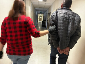 Zdjęcie przedstawia policjantkę ubraną w odzież cywilną, która prowadzi korytarzem zatrzymanego mężczyznę.