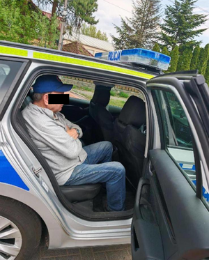 Zdjęcie przedstawia mężczyznę siedzącego na tylnej kanapie radiowozu. Część twarzy ma zasłoniętą czarnym prostokątem.