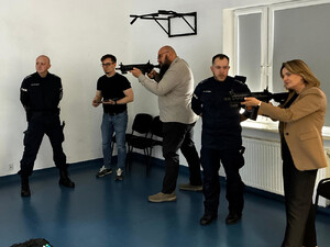 Zdjęcie przedstawia kobietę i mężczyznę celujących z karabinów. Pomiędzy nimi stoi policjant.