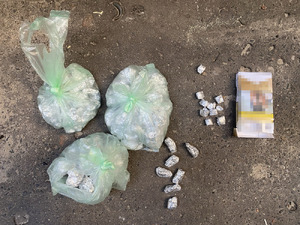 Zdjęcie przedstawia foliowe opakowania z zawartością srebrnych zawiniątek i paczkę po papierosach, leżące na chodniku.