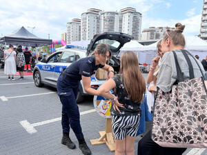 Zdjęcie przedstawia policjantkę, która pochyla się nad dziewczynką, stojącą z matką.