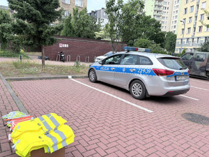 Zdjęcie przedstawia zaparkowany na dziedzińcu szkoły radiowóz i ułożone na ławce materiały odblaskowe.