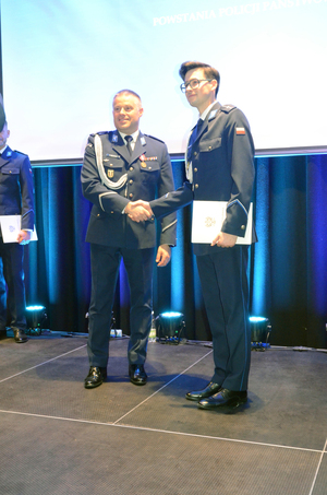 Zdjęcie przedstawia stojącego na scenie I Zastępcę Komendanta Stołecznego Policji i policjanta, pozujących do wspólnego zdjęcia.
