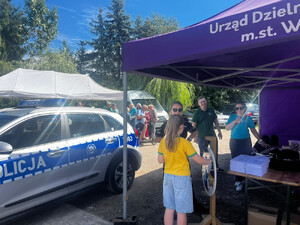 Zdjęcie przedstawia policjantkę stojącą przy kole fortuny z dziewczynką.