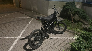 Zdjęcie przedstawia ciemny motorower zaparkowany na miejscu postojowym.